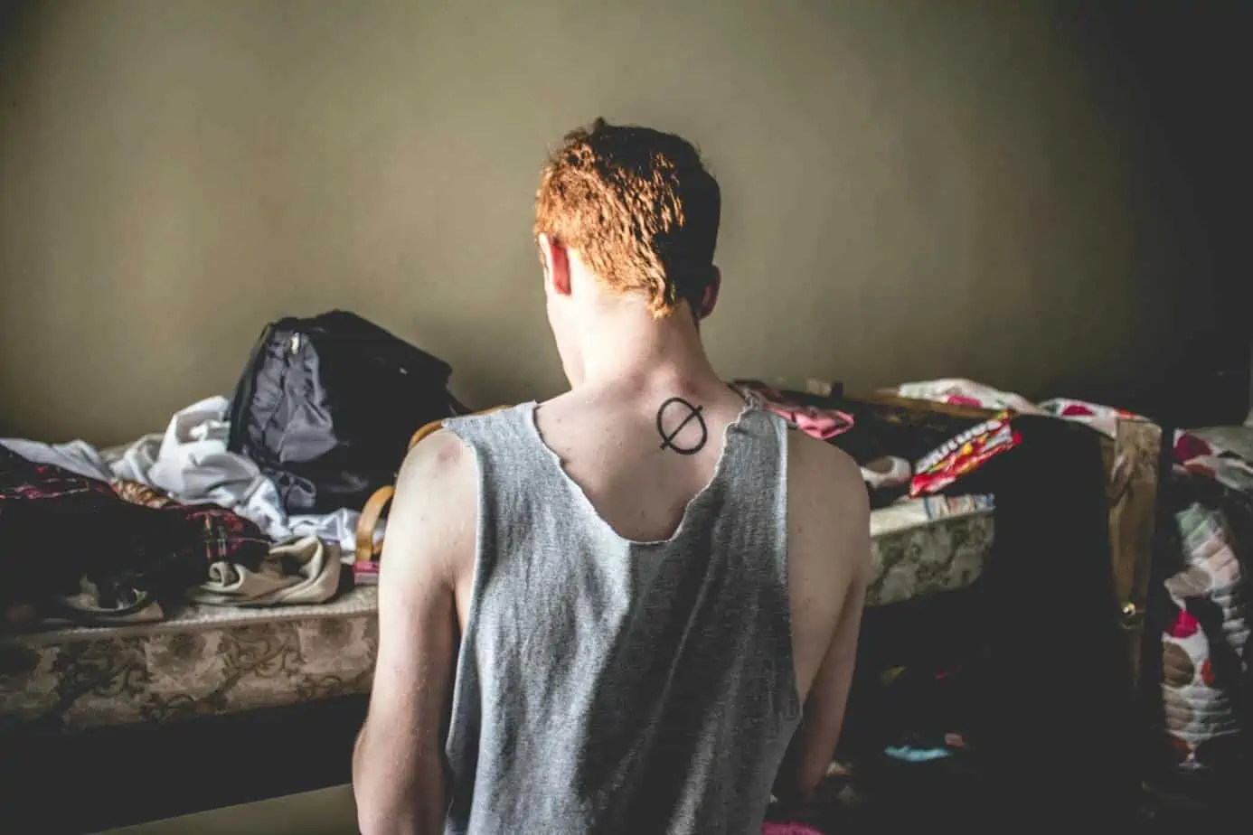 Man with tattoo on neck feels how substance abuse affects his body while looking at a disheveled room