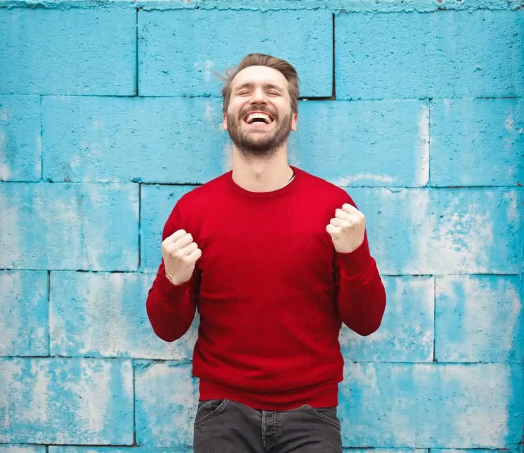 Blonde in red sweater smiling in front of blue brick wall