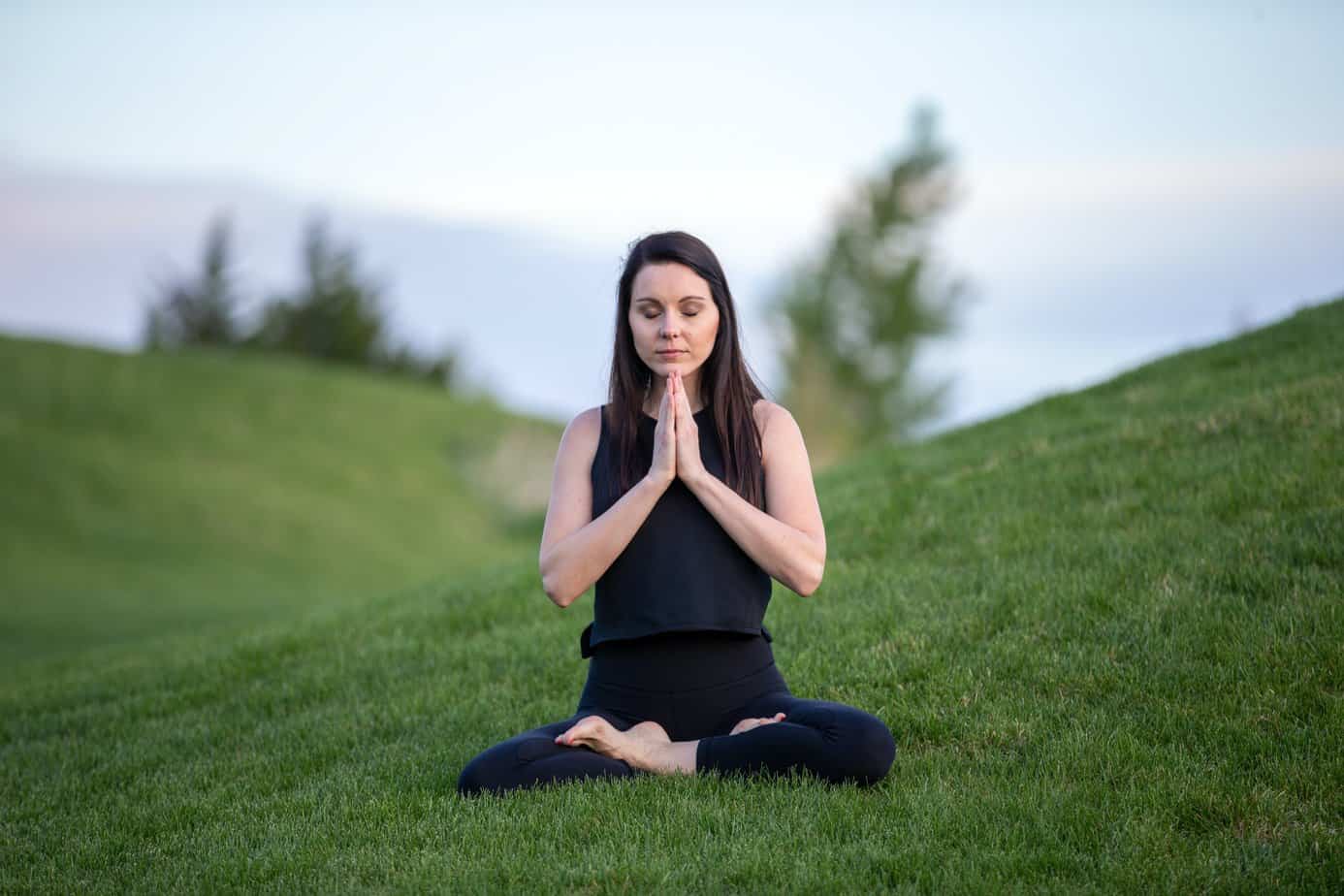 A woman sits on a lawn, meditating.