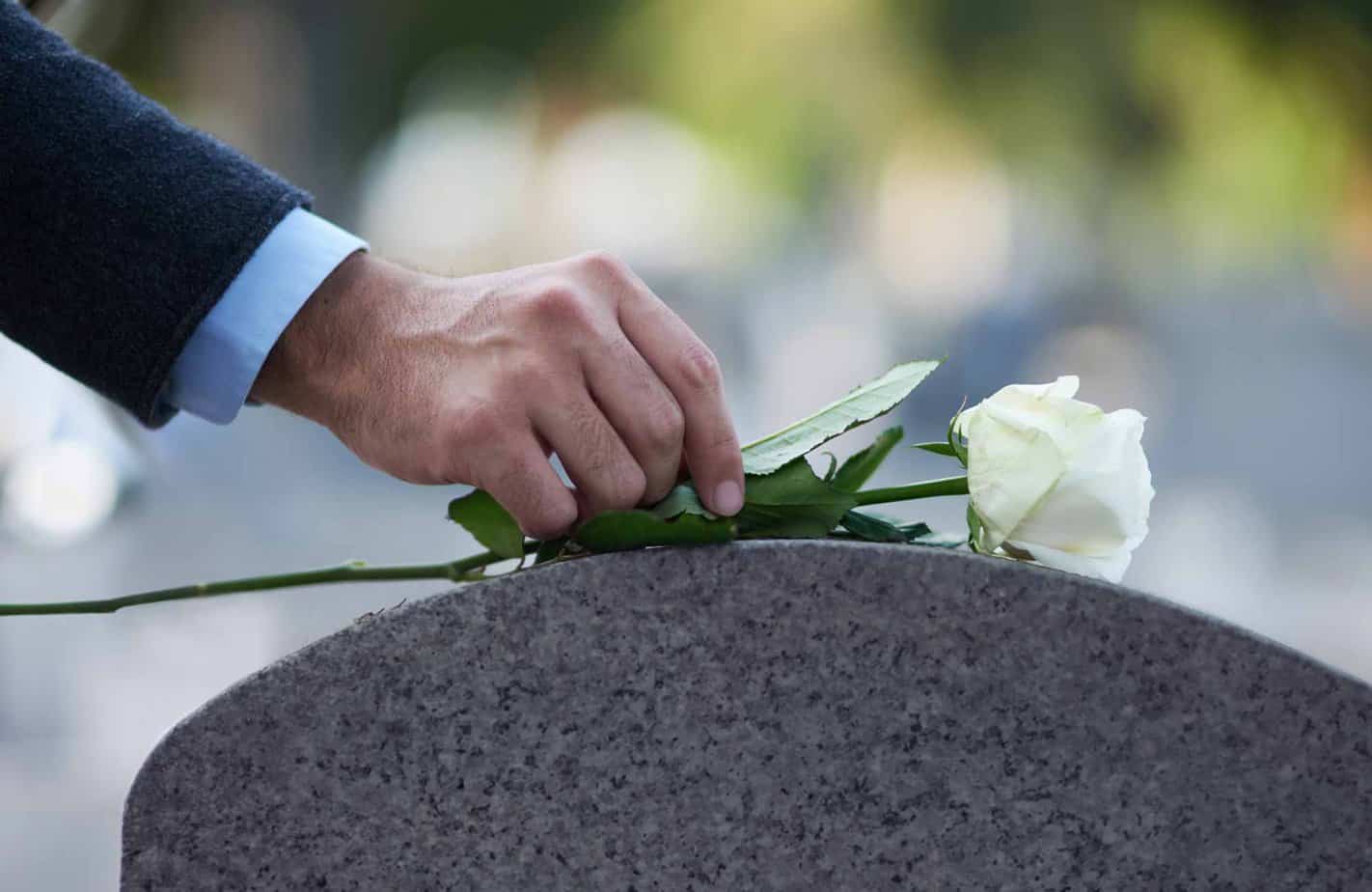 Older man placing white rose on tombstone