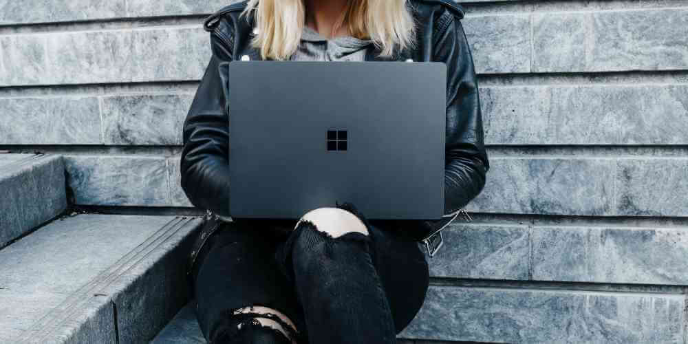 Young girl with blonde hair and leather jacket using a laptop for a support group meeting.