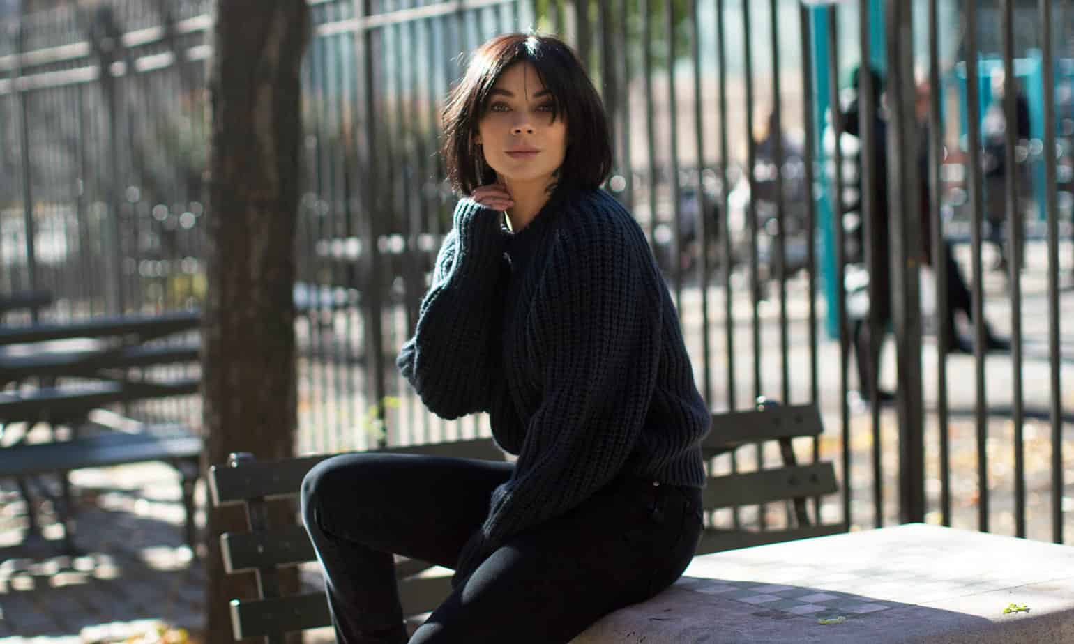 dark haired woman with black sweater and black jeans sitting on table in park