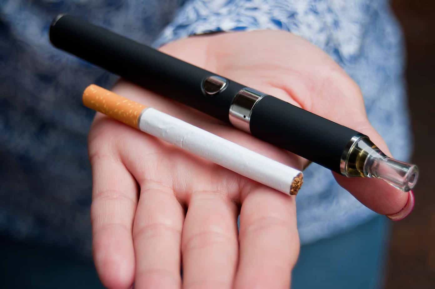 lit cigarette and juul vape pen held in hand