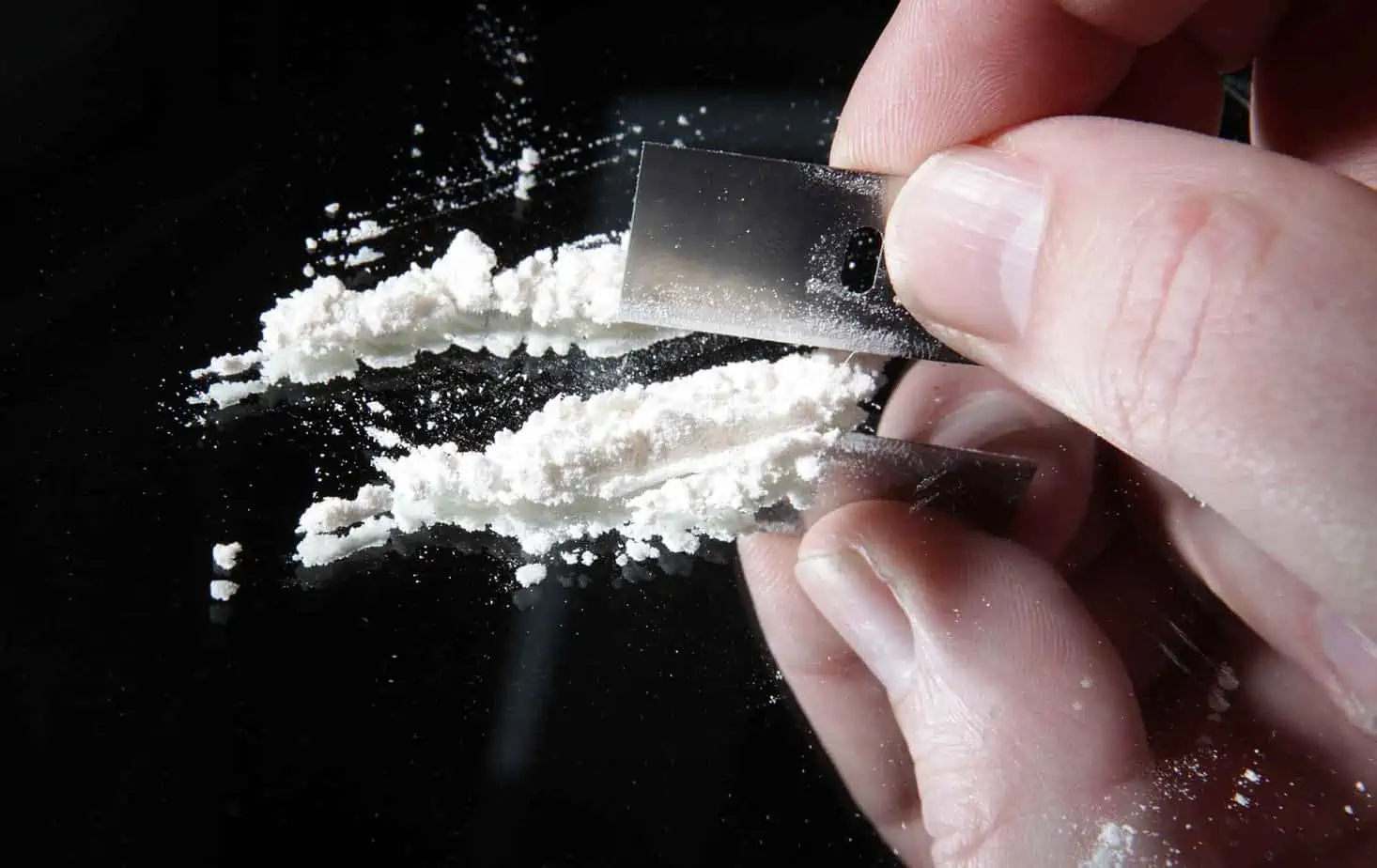 person using razor blade to make cocaine lines