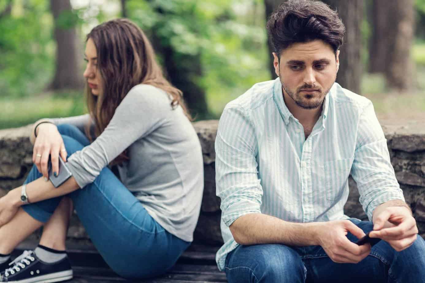 Man and woman sad outside by trees looking away from eachother emotionally distanced