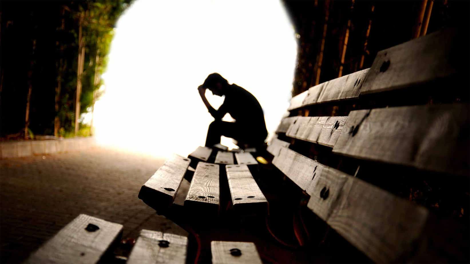 Man holding his head in anguish outside on bench