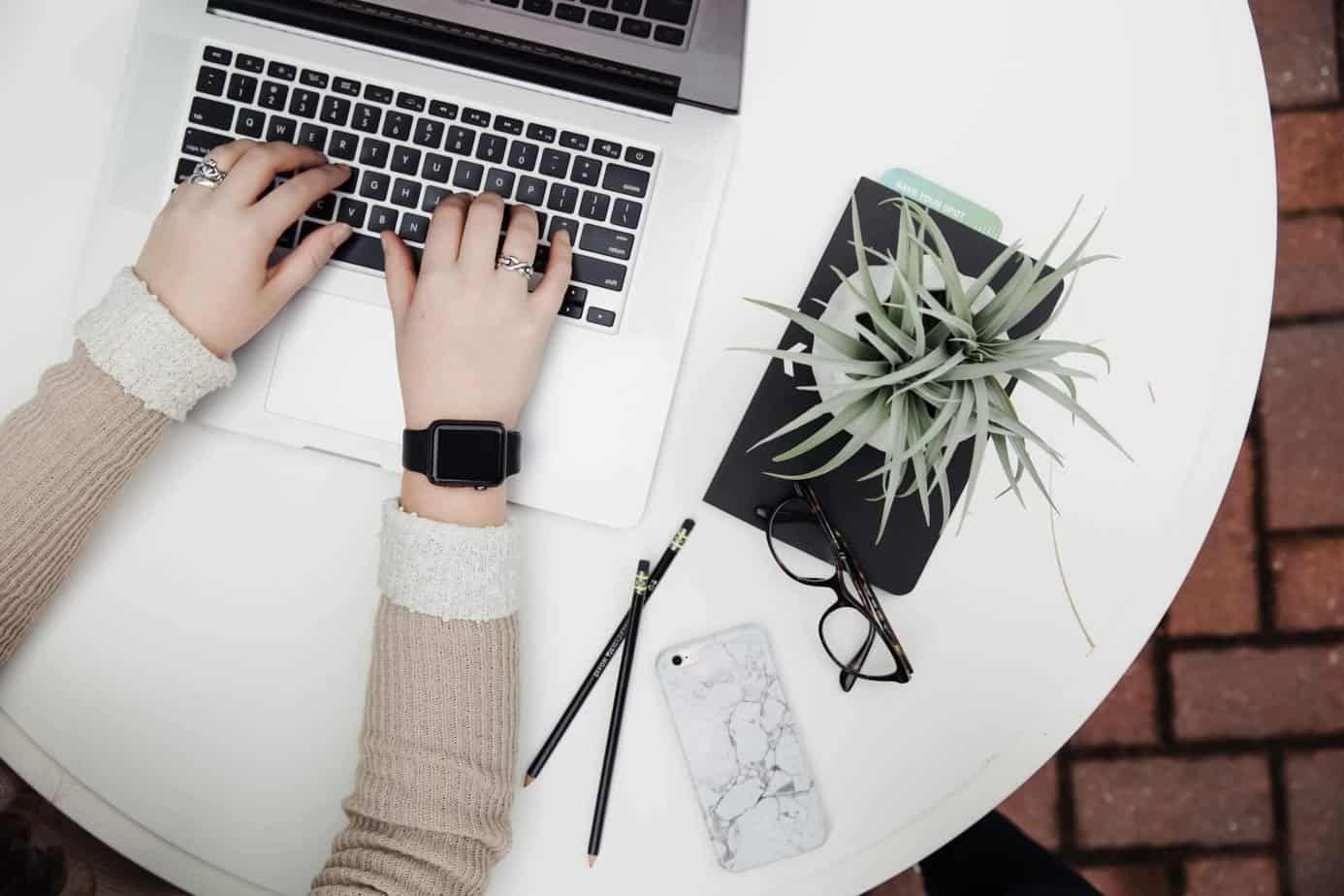 Woman typing on computer with plant and mobile phone nearby