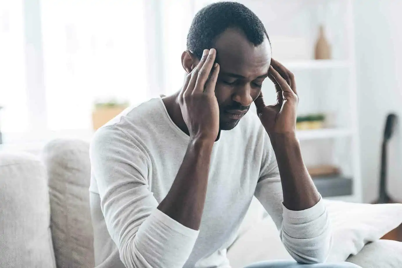 A man with a headache holding his head experiencing detox drug withdrawal symptoms.