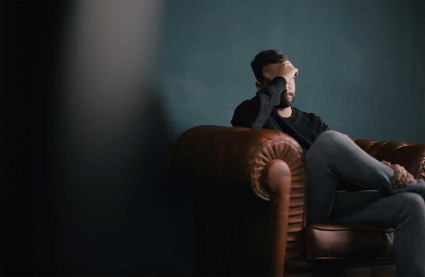 depressed man with head in hands on brown couch