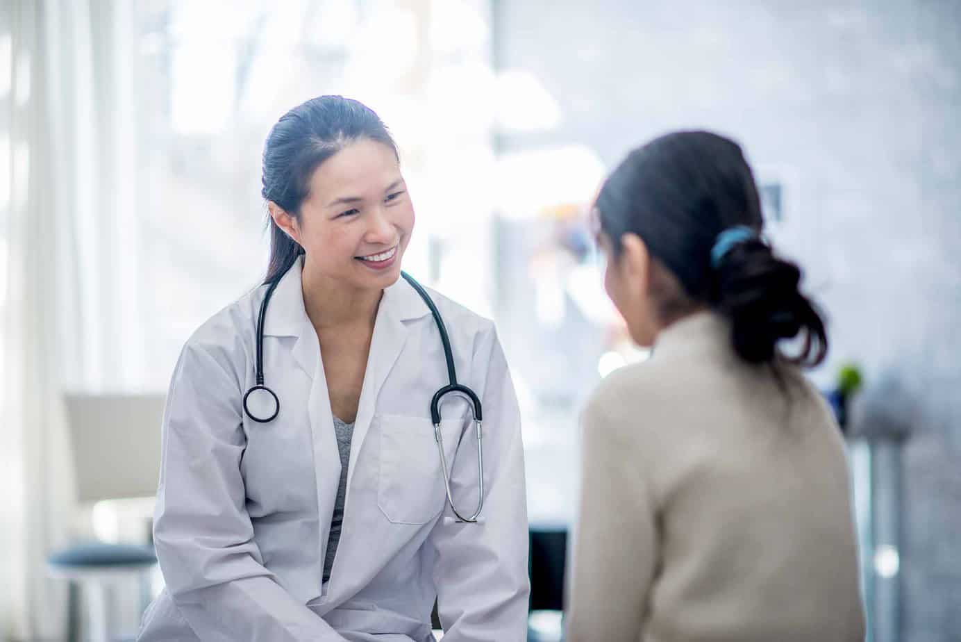 smiling female doctor with stethoscope talking and listening to female patient