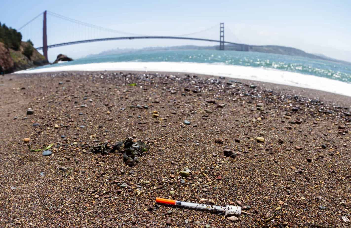 California beach sand with used needle and Golden Gate Bridge and ocean in background