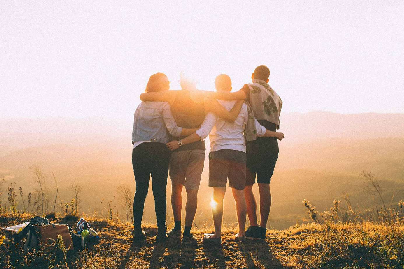 4 men and women arm in arm watching sunset over mountain outside
