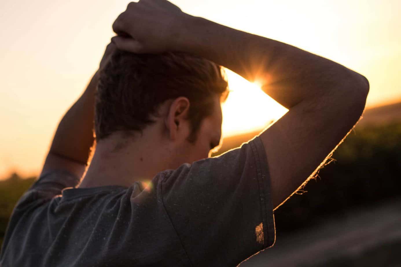 man holding his hair in hands outside with sunset