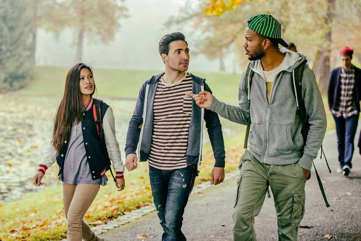 two male and one female college students walking in a line and talking on a college campus