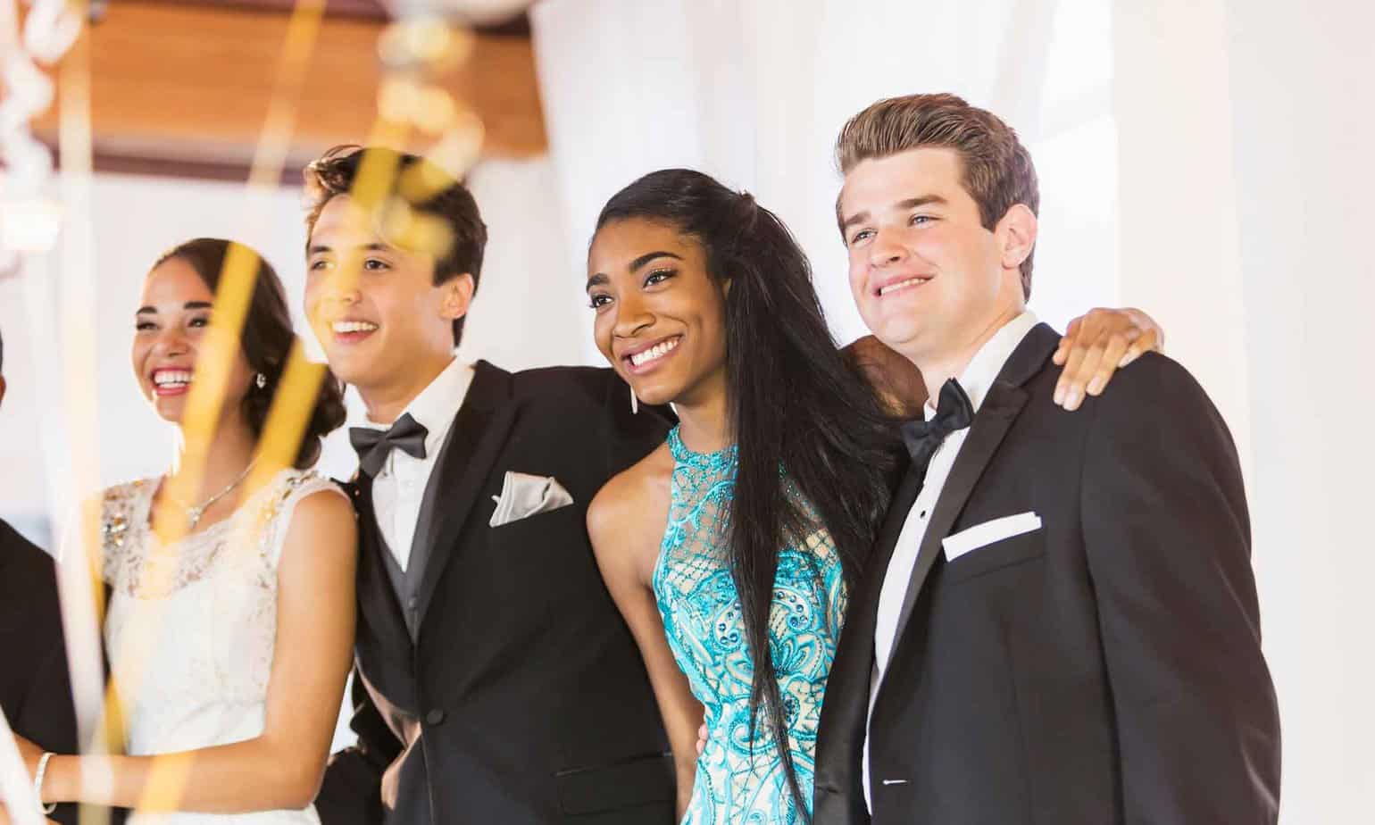 group of teenage high school seniors taking a photo together smiling at prom in dresses and tuxedos