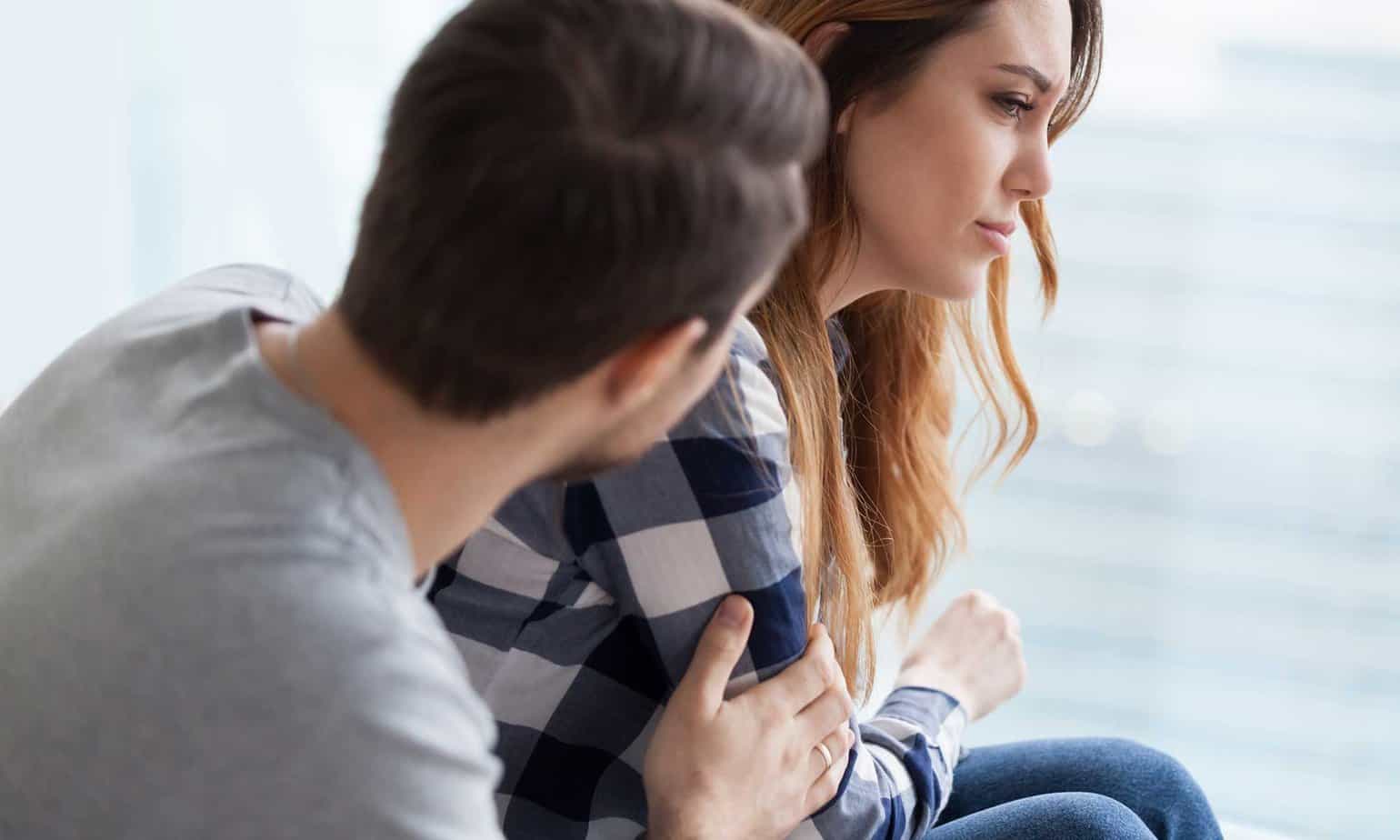 man touching arm of female while she looks away upset