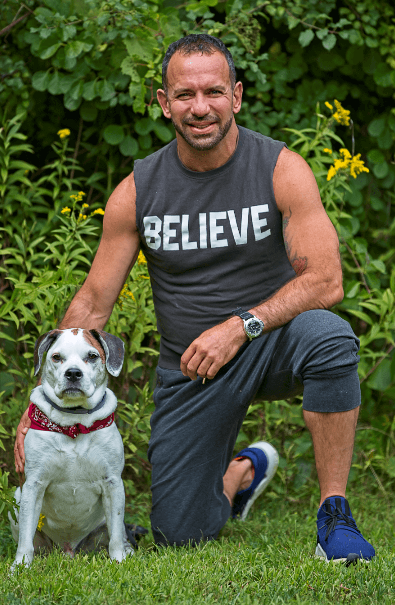 Leandro wearing a believe tshirt kneeling next to a dog wearing a bandana