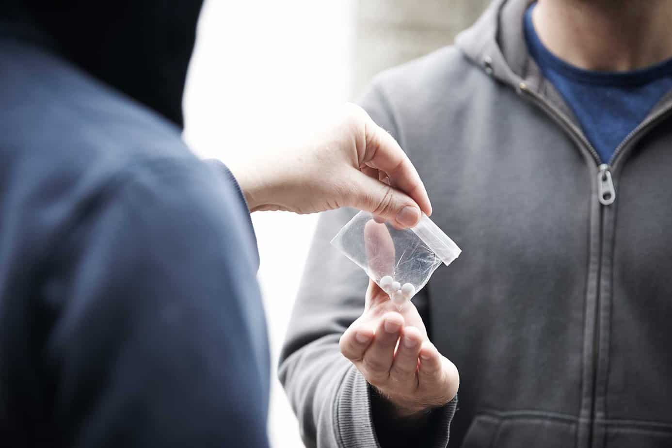person in hoodie giving drugs and pills in plastic bag to man in gray sweatshirt