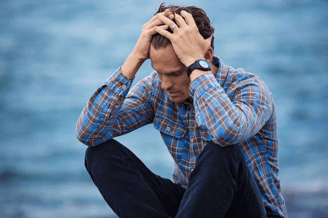 Man sitting by ocean with hands in hair frustrated
