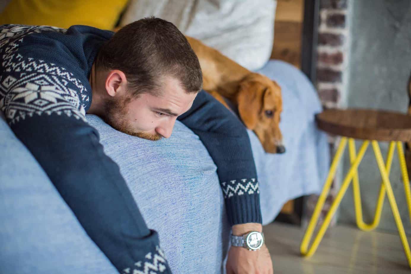 man in sweater lying sideways on bed next to dog