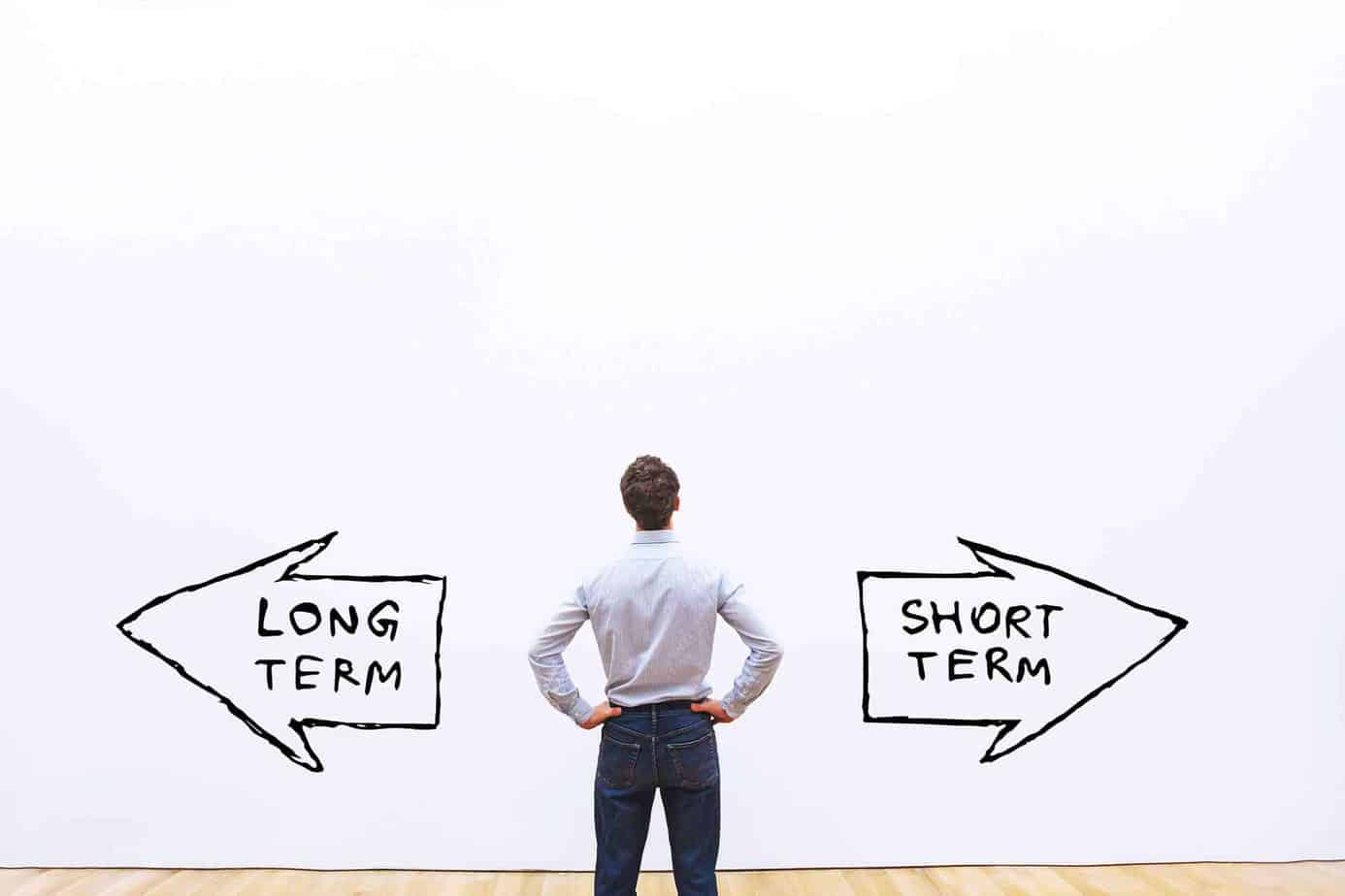 man looking at blank wall with long term and short term arrows pointed in different directions
