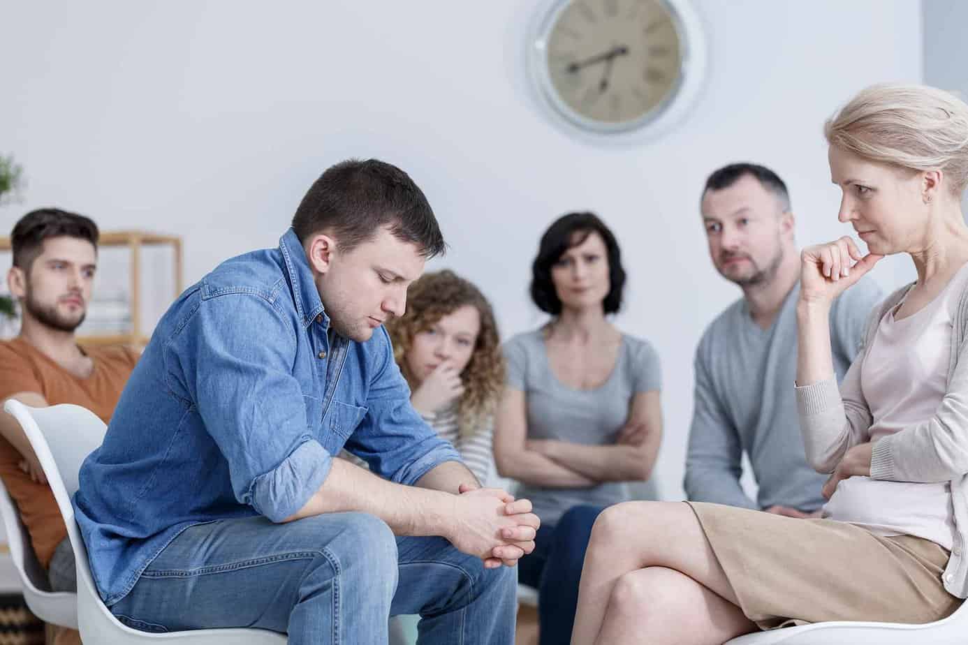 man looking down sad with hands clasped in a support group with therapist