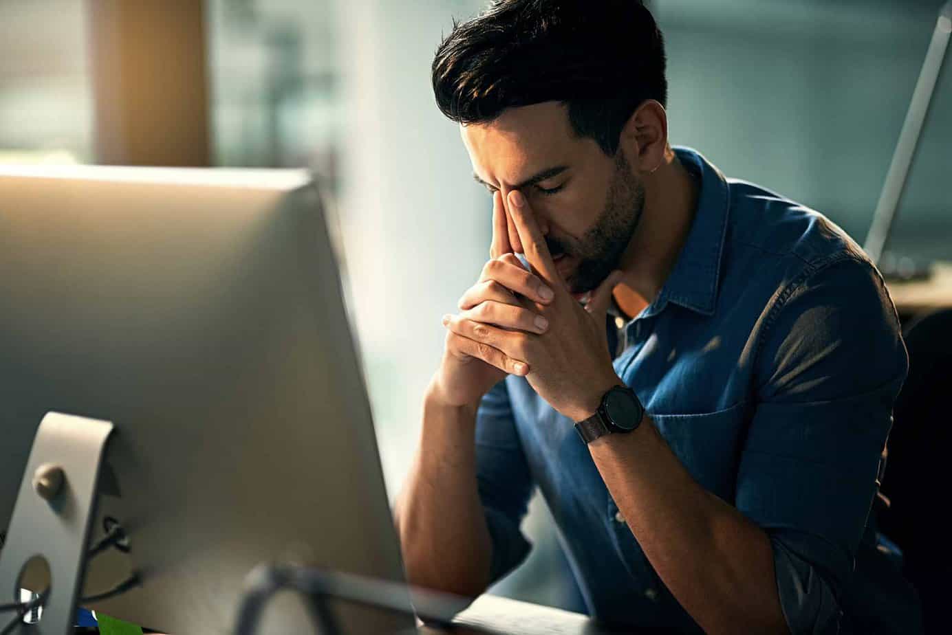 stressed man sitting in front of computer with hands on face