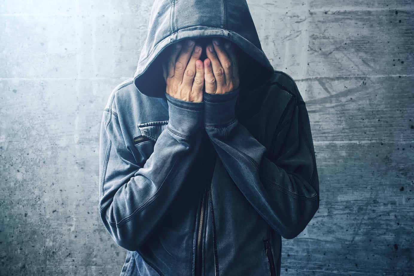 man in hoodie with hands covering face struggling with heroin addiction
