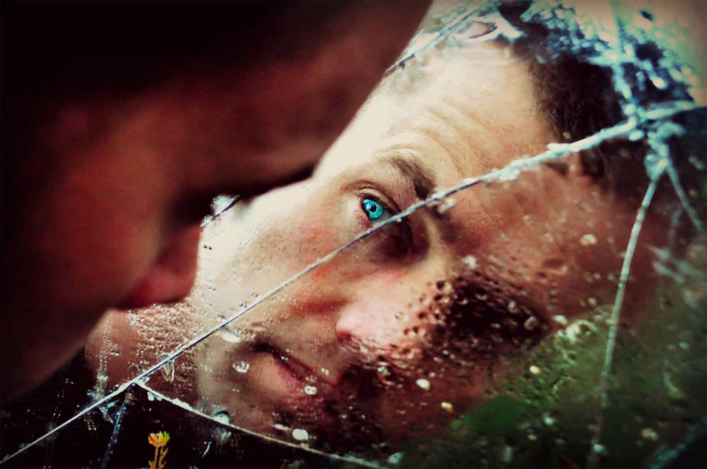 man with blue eyes staring into reflection in a cracked and broken mirror