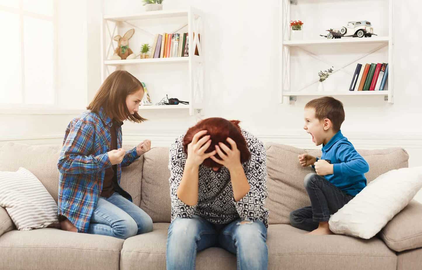 mother holding her head in frustration as two kids argue on both sides of her