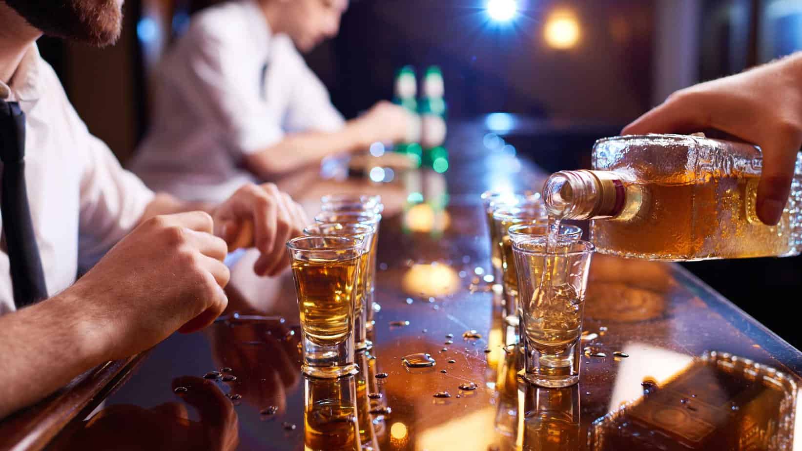 shot glasses with liquor on bar countertop and bartender pouring out liquor