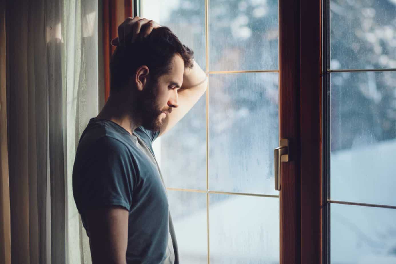 depressed man looking out the window holding his head