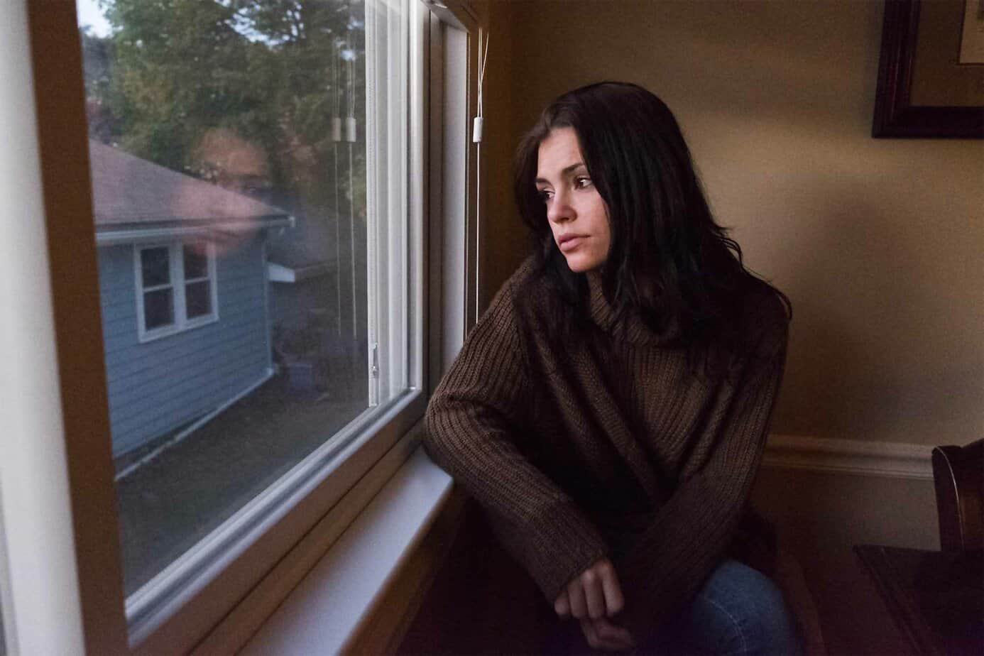 A sad woman looks out of a window