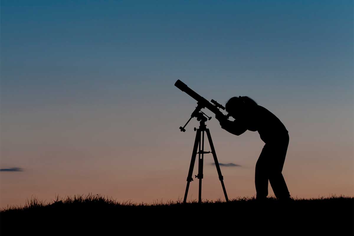 silhouette of person gazing at night sky through a telescope