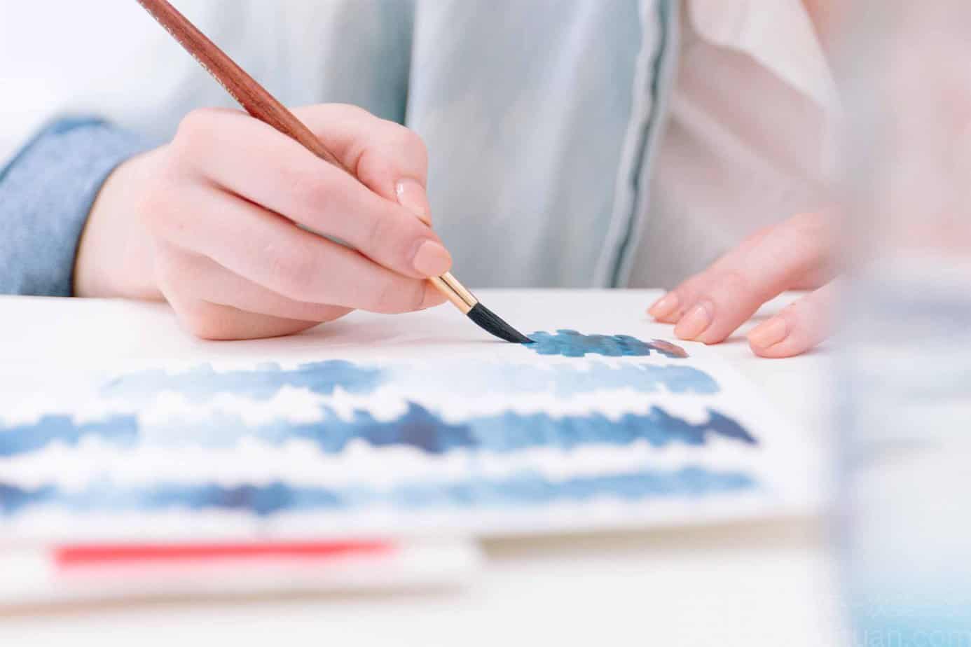 person painting with watercolors on canvas