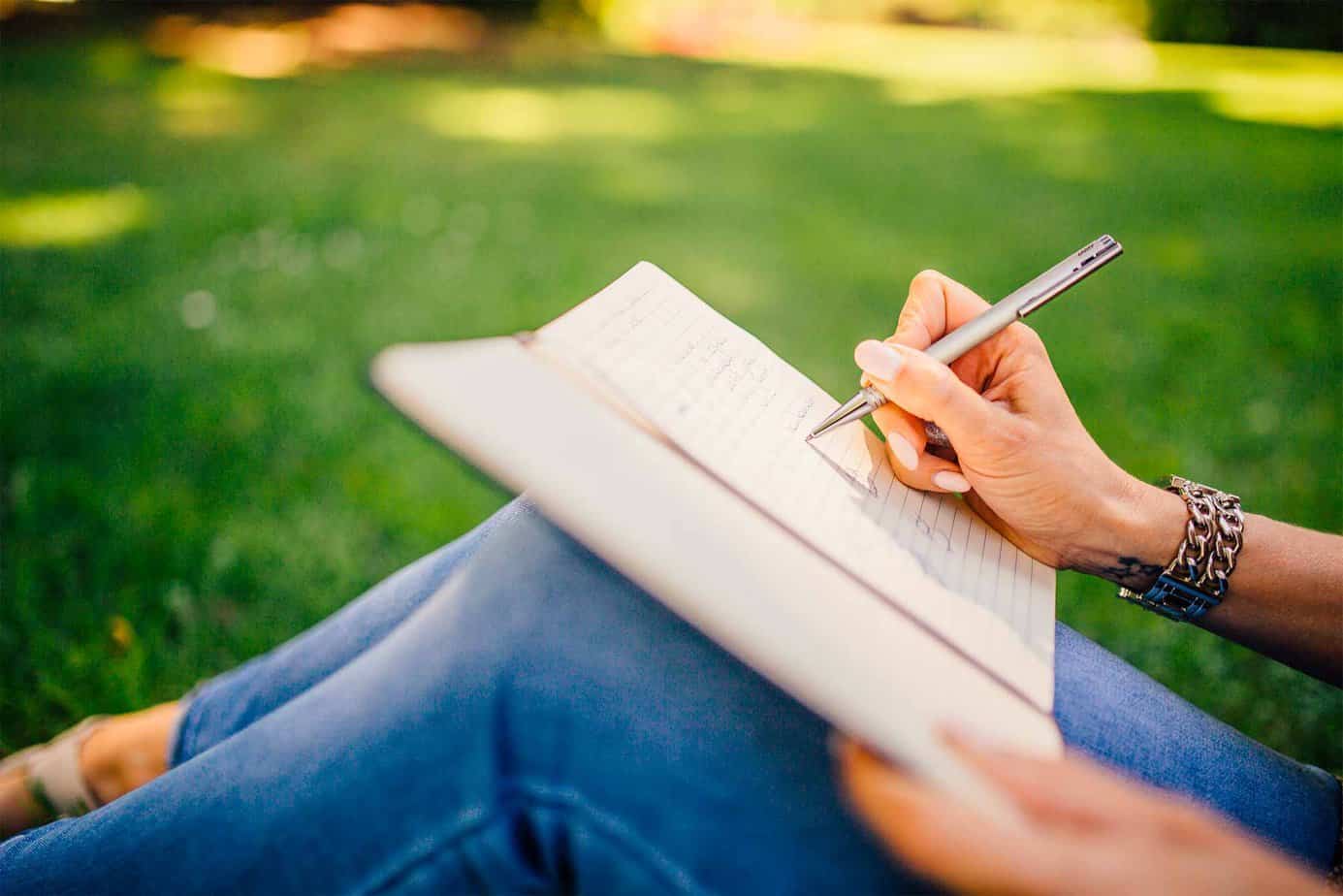 person writing in journal outside on the grass