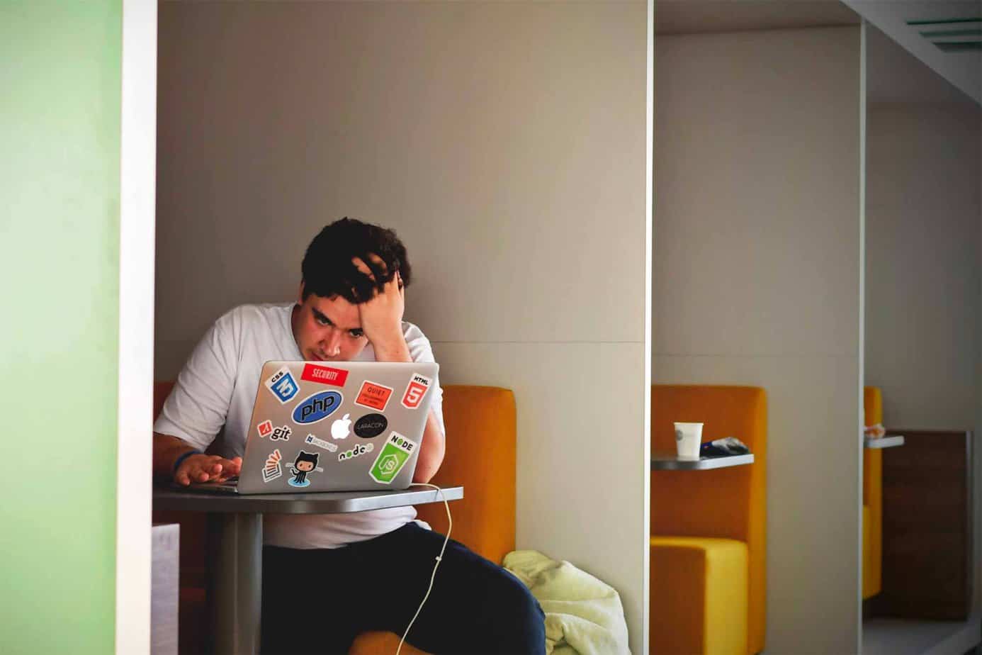 man stressing over his gambling addiction as he holds his head staring at computer