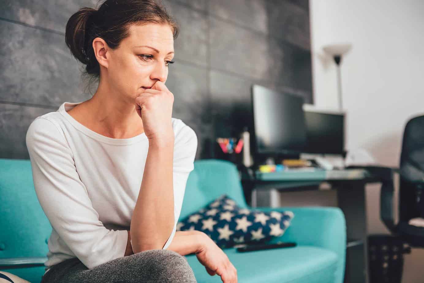 worried woman sitting on the couch with hand on her chin