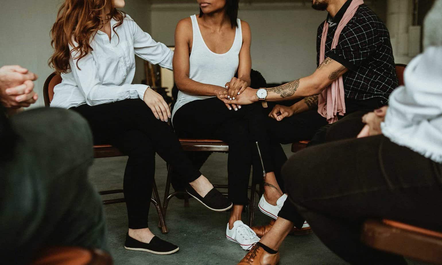 Three young individuals attending an AA meeting supporting and comforting each other