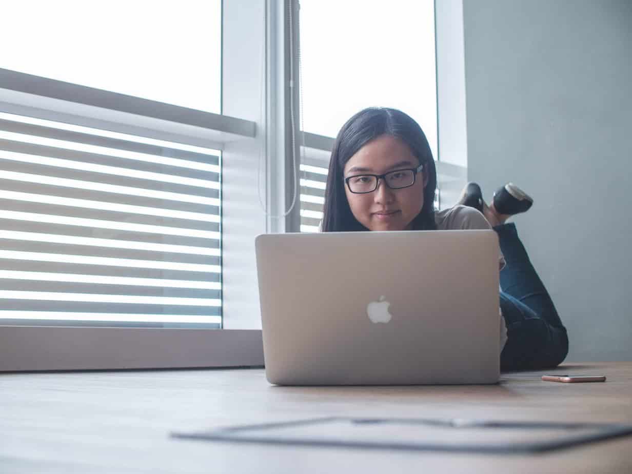 An asian woman with dark hair and glasses using a Macbook Pro laptop.