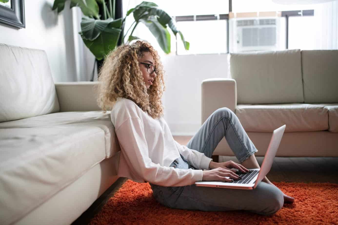 A woman of color with curly blonde hair, using a laptop in her living room.