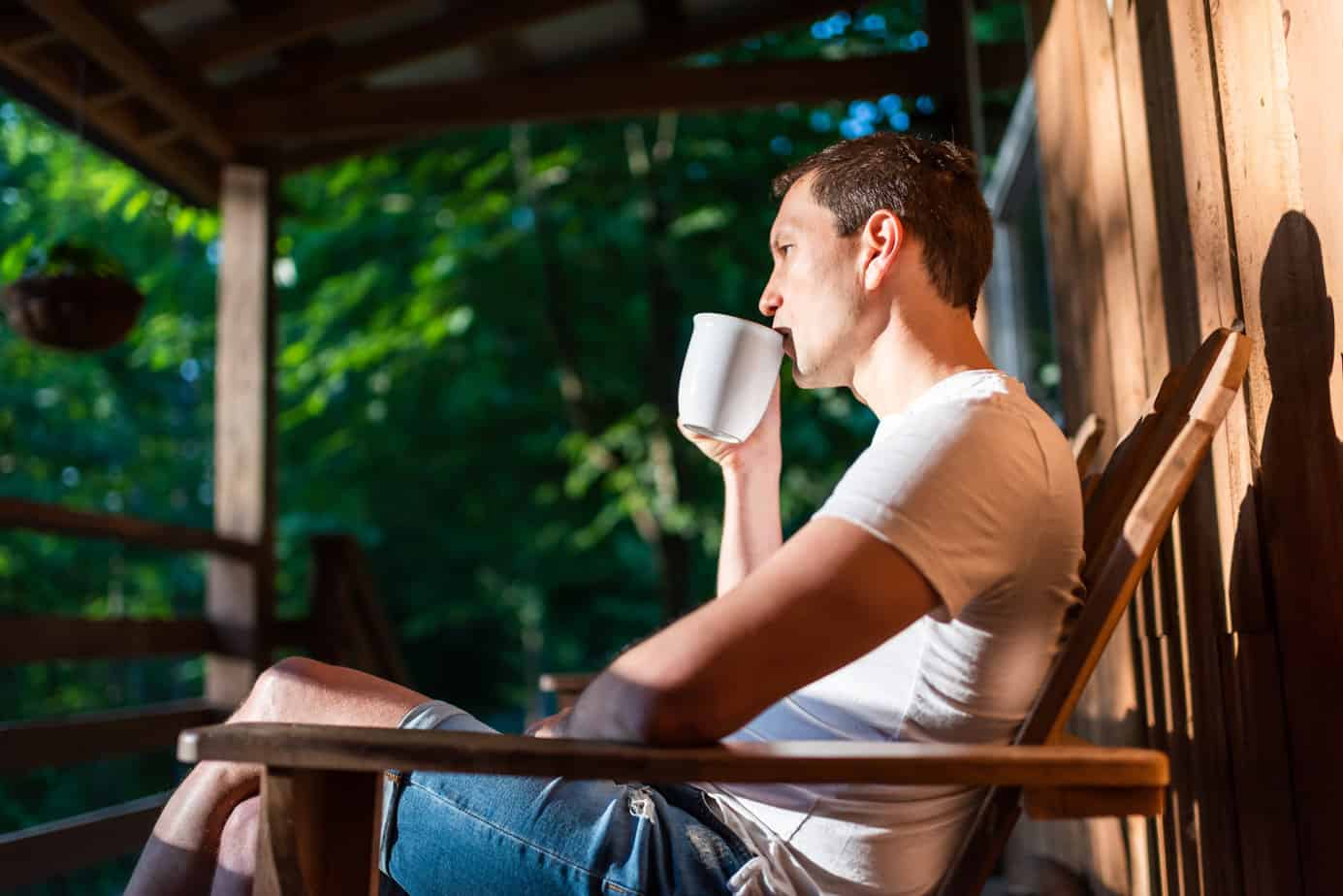 man sitting on porch outside drinking coffee
