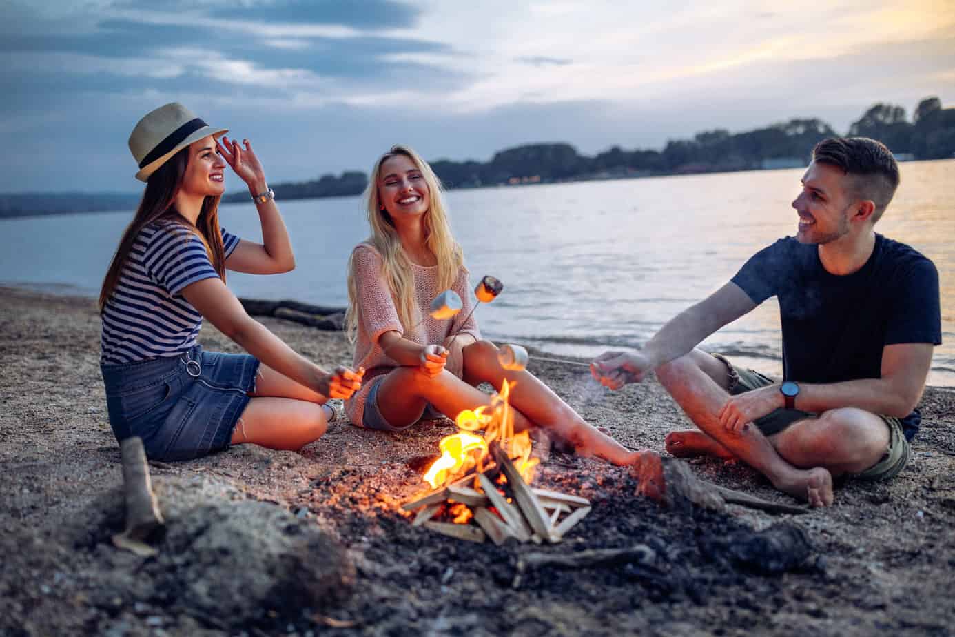 friends sitting around campfire roasting marshmallows on a beach