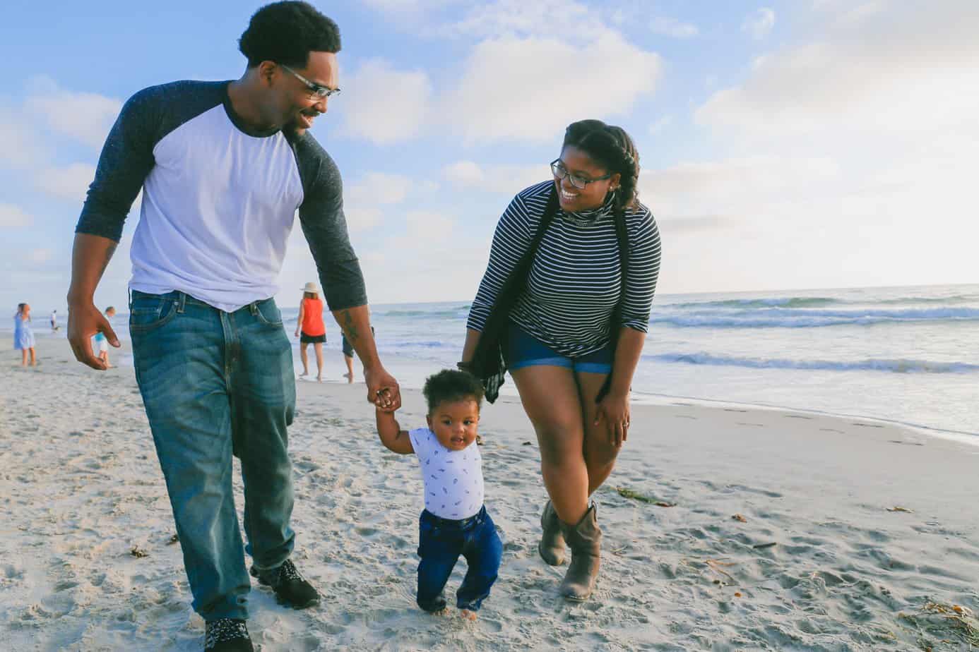 A family of three explores a beach; mom and dad hol donto the hands of their child