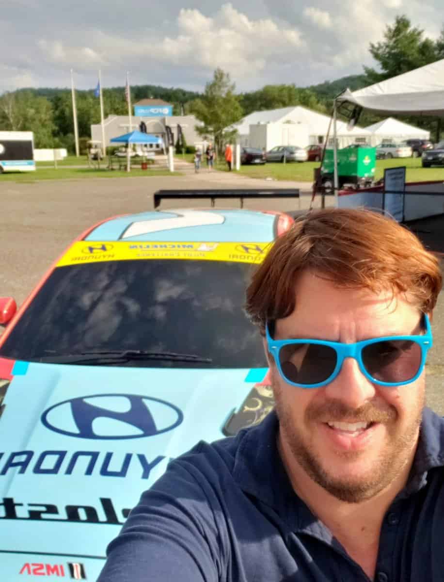 Man smiling behind race car at Mountainside Treatment Center Extended Care Lime Rock Park Event Summer 2022