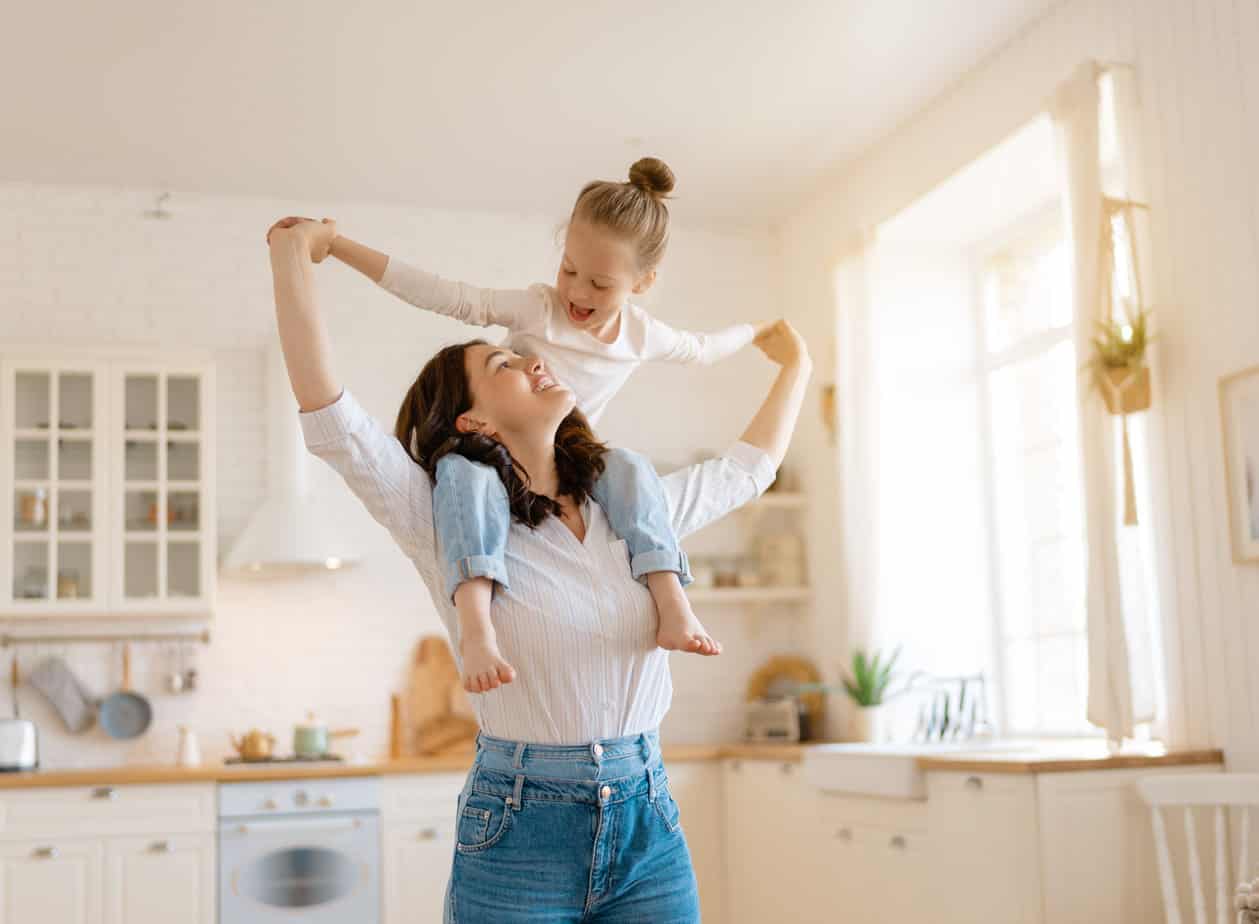 mom with daughter sitting on shoulders smiling and holding hands