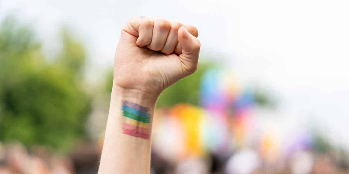 man raising arm with LBGT flag in support at a rally